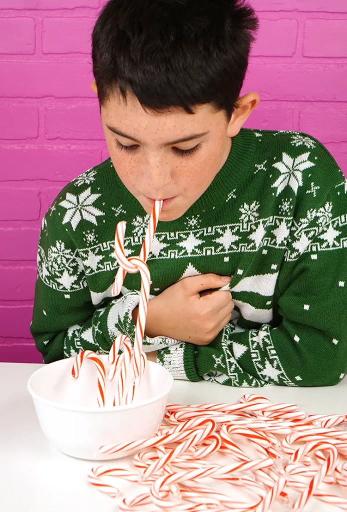 A boy participating in the game "Candy Cane Hook 'Em - a fun and challenging Minute to Win It game for Christmas parties.