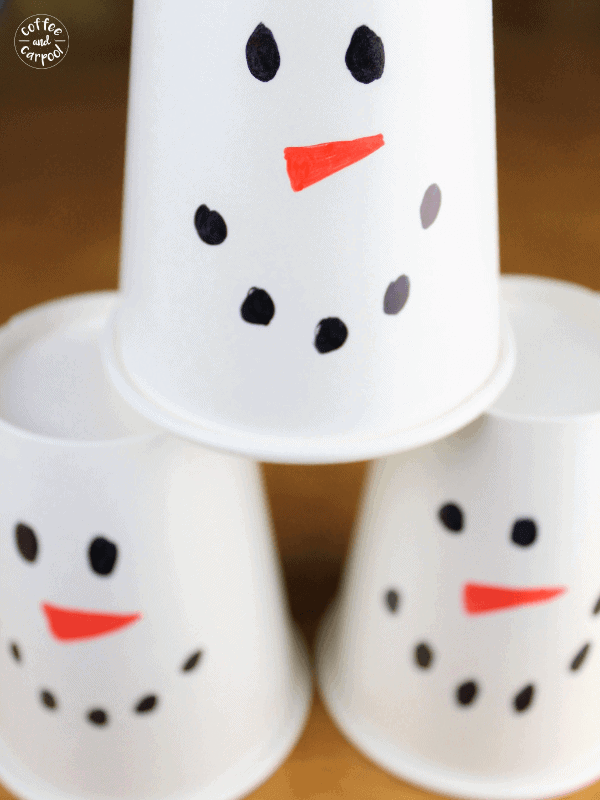 White plastic cups with snowman faces drawn on them stacked to be knocked down in a Christmas-themed bowling game.